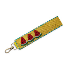 Load image into Gallery viewer, Hand beaded watermelon wristlet keychain featuring three colorful watermelon slices on a mustard yellow beaded strap with turquoise trim. Includes a gold-tone lobster clasp and soft wrist loop, perfect for carrying keys, key fobs, ID badges, or small accessories.