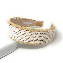 Load image into Gallery viewer, A white woven headband with a beige lace trim, resting on a white block against a white background. The inner band shows the brand name 'Tocade'.