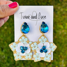 Load image into Gallery viewer, Pair of floral earrings with blue stones on a &#39;Twine and Love&#39; branded card, held against a green outdoor background.