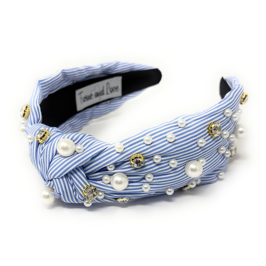 A blue and white striped headband adorned with pearls and gold beads. It features a knot design, creating an elegant and stylish accessory.