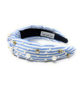 A stylish headband with blue and white stripes, adorned with pearls and sparkling gems. It has a knotted design, offering a chic and elegant look.
