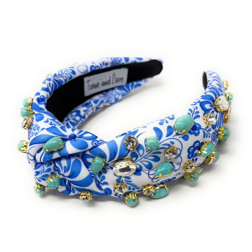 A blue and white floral-patterned headband adorned with turquoise stones and sparkling gems. It conveys a vibrant, elegant, and artistic flair.