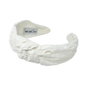 White headband with intricate white floral embroidery, displayed in a side view. The soft texture and elegant design convey a stylish, timeless appeal.