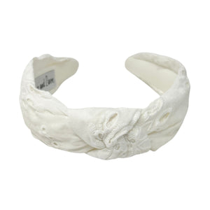 White headband with intricate white floral embroidery, displayed in a side view. The soft texture and elegant design convey a stylish, timeless appeal.