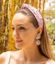 Load image into Gallery viewer, Woman wearing a pink headband with decorative elements and gold earrings outdoors.