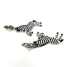 Load image into Gallery viewer, Woman wearing whimsical zebra dangle earrings with detailed striped bead embroidery and floral stud accents.