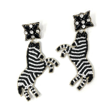 Load image into Gallery viewer, Black and white zebra-shaped beaded earrings worn by a model, featuring intricate stripe detailing and statement dangle design.