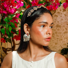 Load image into Gallery viewer, A stylish woman wearing a white dress with buttons and statement earrings, surrounded by vibrant flowers.
