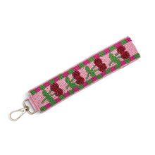 Load image into Gallery viewer, Side view of a handcrafted cherry beaded wristlet keychain with a pink background, green checker border, and gold-tone lobster clasp.