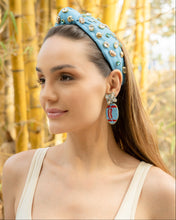 Load image into Gallery viewer, A woman wearing a stylish Football blue headband adorned with jewels and colorful earrings in a natural setting.