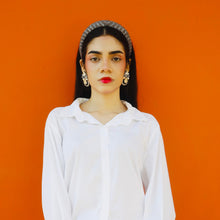 Load image into Gallery viewer, A model showcasing elegant statement earrings against an orange background.