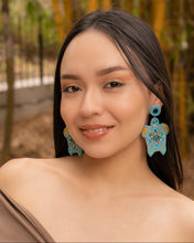 Load image into Gallery viewer, Close-up of a woman wearing elegant beaded turtle earrings in a natural setting.