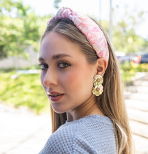 Load image into Gallery viewer, A woman elegantly styled with a pink headband and decorative flower earrings in a sunny outdoor setting.