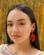 Load image into Gallery viewer, Close-up portrait of a woman wearing elegant red earrings against a bamboo backdrop.
