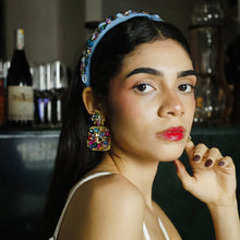 Load image into Gallery viewer, A close-up portrait of a woman with a stylish headband and colorful earrings, showcasing her makeup and expression.
