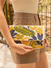 Load image into Gallery viewer, A woman holding a colorful floral clutch bag in a sunny outdoor setting.