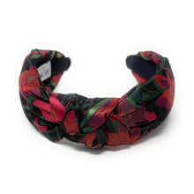 Load image into Gallery viewer, A colorful, padded headband with a floral pattern in red, green, and black hues. The fabric is twisted at the front, creating a knot-like design.