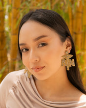 Load image into Gallery viewer, Model showcasing gold nurse earrings in a natural setting.