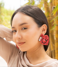 Load image into Gallery viewer, Close-up of a woman wearing heart-shaped beaded earrings in a natural setting.
