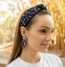 Load image into Gallery viewer, A woman wearing a stylish navy headband adorned with colorful gems and unique football-shaped earrings.