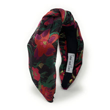 Load image into Gallery viewer, A colorful, padded headband with a floral pattern in red, green, and black hues. The fabric is twisted at the front, creating a knot-like design.