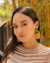 Load image into Gallery viewer, Model showcasing vibrant pineapple earrings against a natural backdrop.