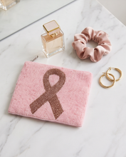 Load image into Gallery viewer, A pink beaded zipper pouch featuring a brown beaded awareness ribbon, styled on a white marble surface alongside a pink satin scrunchie, gold hoop earrings, and a perfume bottle.