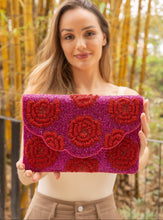 Load image into Gallery viewer,  A stylish red rose beaded clutch held by a woman in a natural setting.