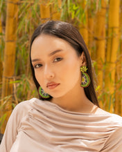 Load image into Gallery viewer, Close-up of a woman wearing vibrant earrings against a bamboo background.
