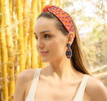 Load image into Gallery viewer, A young woman wearing a vibrant orange headband with blue embellishments and stylish earrings, set against a backdrop of bamboo.