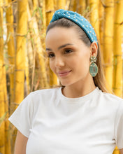 Load image into Gallery viewer, A woman wearing a blue headband with pearls and large earrings, standing in front of bamboo.