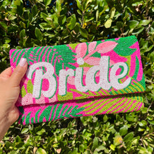 Load image into Gallery viewer, Handmade bride clutch purse with vibrant beadwork, pink floral accents, and bold white lettering, styled with casual denim and a white top.