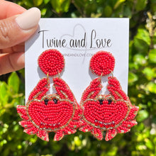 Load image into Gallery viewer, Red beaded crab earrings handcrafted with intricate beadwork, gold accents, and playful coastal-inspired detailing against a leafy outdoor background.