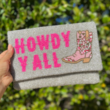 Load image into Gallery viewer, Model in a black dress carrying a handmade beaded envelope clutch that reads “Howdy Y’all” in vibrant pink beads.